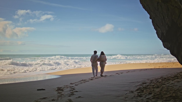 Des époux insouciants marchant sur le sable de la plage fuyant l'océan un couple romantique