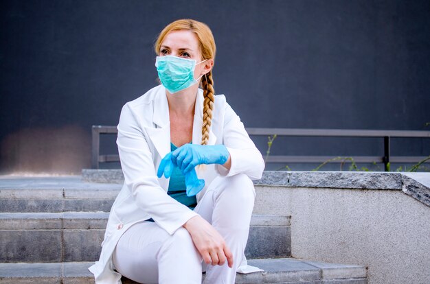 Photo Épuisé, femme médecin, séance, devant, clinique, regarder loin., fatigué, femme, infirmière, délassant, sur, escalier hôpital., covid-19, virus, mondiale, pandémie