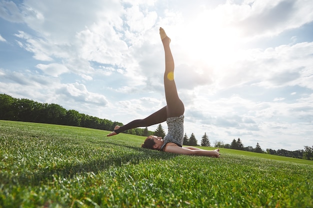 L'équilibre du yoga exerce une jeune femme en vêtements de sport pratiquant le yoga asana sur une pelouse verte