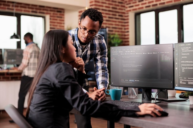 Équipe d'administrateurs de base de données déboguant l'algorithme travaillant dans un bureau de développement de logiciels. Deux programmeurs cloud analysant le code source sur un écran d'ordinateur, comparant le script de données dans un bureau d'agence occupé.