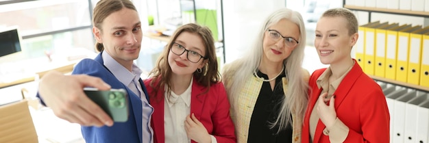 Une équipe d'affaires heureuse prend un selfie sur un smartphone dans un bureau d'entreprise, un employé prend une photo