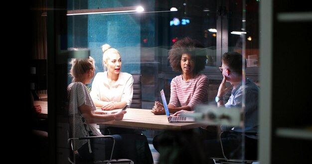 Équipe d'affaires multiethnique en démarrage lors d'une réunion dans un brainstorming intérieur de bureau de nuit moderne, travaillant sur un ordinateur portable