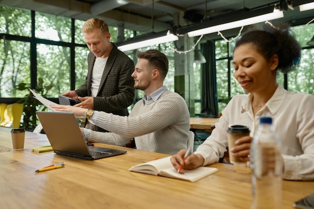 Une équipe d'affaires multiethnique heureuse discutant, travaillant ensemble dans un espace ouvert de bureau de coworking.