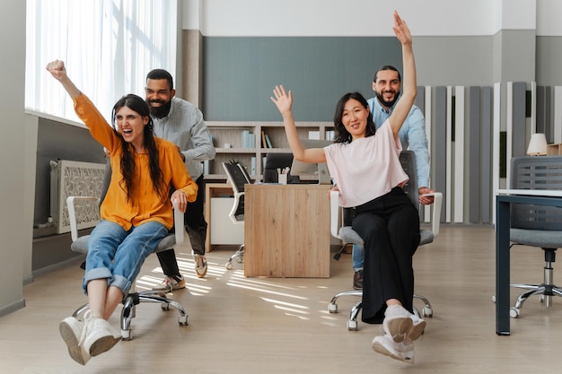 Une équipe d'affaires multiethnique heureuse qui s'amuse à courir sur des chaises au bureau.