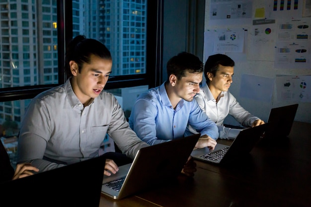 équipe d&#39;affaires travaillant tard dans la nuit avec les lumières éteintes et les ordinateurs d&#39;ordinateur portable allument la lumière.