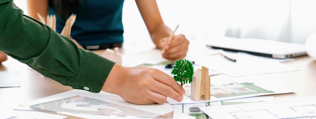 Une équipe d'architectes professionnels discute de la conception verte d'une maison écologique sur une table de réunion avec un plan et un modèle dispersés autour de Closeup Focus sur la main Concept de ville verte Définition
