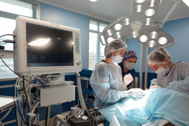 Équipe Chirurgicale Concentrée Opérant Un Patient Dans Une Salle D'opération. Un Anesthésiste Bien Formé Avec Des Années De Formation Avec Des Machines Complexes Suit Le Patient Tout Au Long De La Chirurgie.