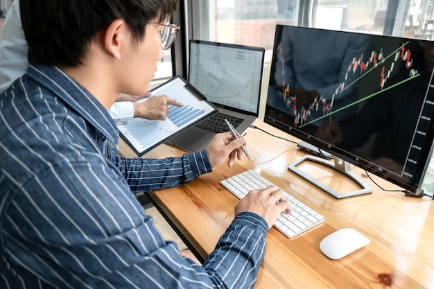 Photo Équipe de commerçants d'affaires vérifiant le marché boursier en ligne analysant les données graphiques sur l'écran d'un ordinateur portable pour réfléchir au commerce en ligne tout en travaillant ensemble au bureau