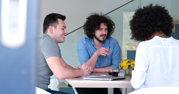 Photo Équipe commerciale de démarrage multiethnique lors d'une réunion dans un brainstorming intérieur de bureau moderne et lumineux, travaillant sur un ordinateur portable et une tablette