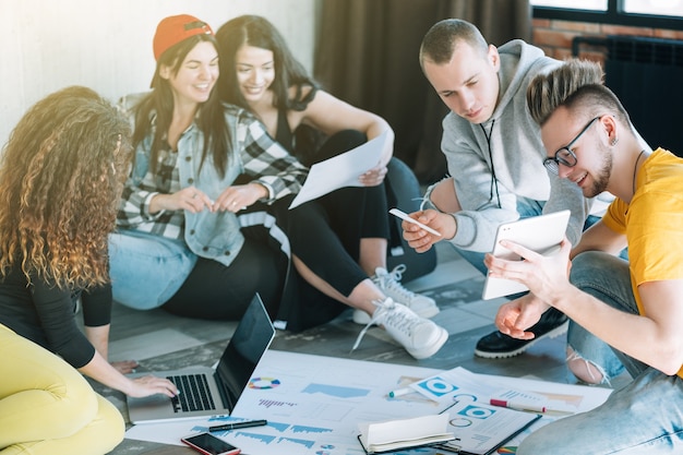 équipe commerciale millénaire travaillant ensemble. groupe de jeunes diversifié assis sur le sol.