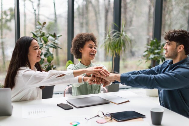 Équipe commerciale multiethnique célébrant le succès en se donnant la main à l'intérieur du bureau