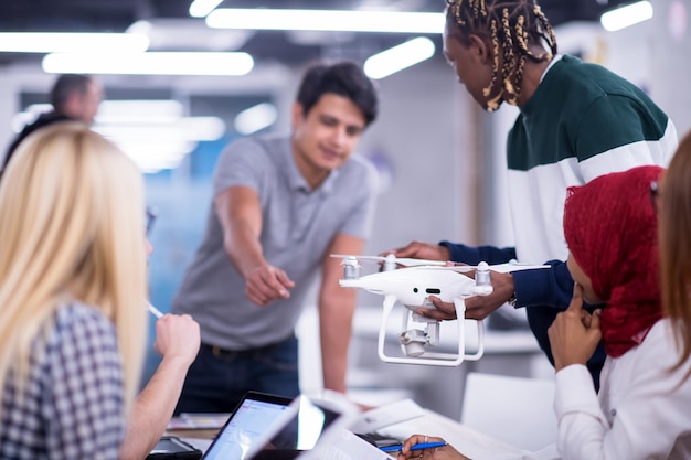 une équipe commerciale multiethnique en démarrage discute d'un nouveau plan d'affaires, travaille sur un ordinateur portable et une tablette tout en se familiarisant avec la technologie des drones pour l'avancement de nouvelles entreprises