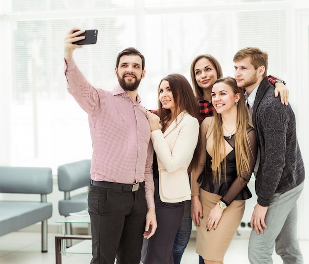 équipe commerciale professionnelle faisant selfie tout en se tenant près de la fenêtre dans un bureau moderne