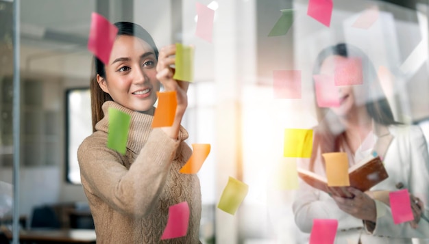 équipe créative de femme d'affaires utilisant des post-it dans un mur de verre pour écrire un plan d'affaires stratégique