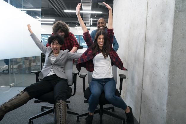 équipe de démarrage multiethnique de développeurs de logiciels s'amusant tout en courant sur des chaises de bureau, des employés divers excités riant en profitant d'une activité amusante pendant la pause de travail, des travailleurs créatifs et sympathiques p