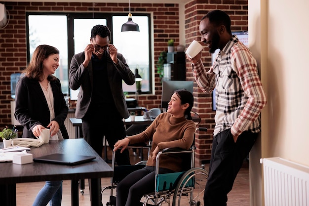 Photo une équipe diversifiée de collègues riant dans un bureau d'affaires avec une femme paralysée assise en fauteuil roulant. employé asiatique souffrant d'un handicap chronique et d'une déficience s'amusant avec ses collègues.