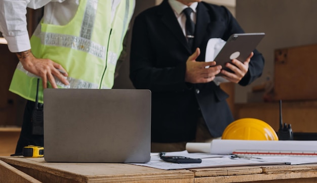 Une équipe diversifiée de spécialistes utilise un ordinateur tablette sur le chantier de construction d'un projet immobilier avec un ingénieur civil, un architecte d'entreprise, un investisseur et un ouvrier général discutant des détails du plan