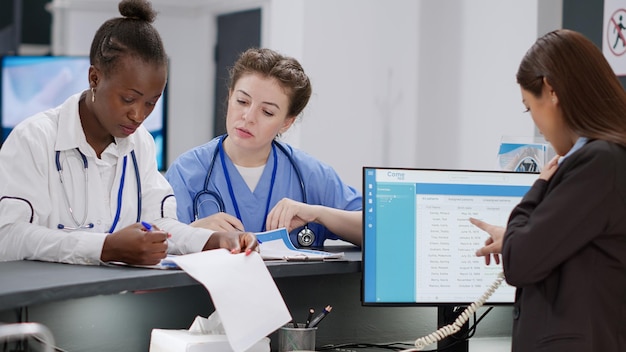 Photo une équipe diversifiée de travailleurs médicaux analysant les rapports de contrôle et les rendez-vous avec l'assurance. infirmière, médecin et réceptionniste travaillant sur des formulaires à la réception de l'hôpital, aide à la consultation.