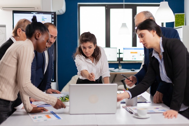 Équipe Diversifiée De Travailleurs Parlant, Regardant Des Documents Et Analysant Des Données Graphiques Se Tenant Au Bureau De La Conférence. Collègues Multiethniques Travaillant à La Planification De La Stratégie Financière Du Succès Discutant Au Bureau