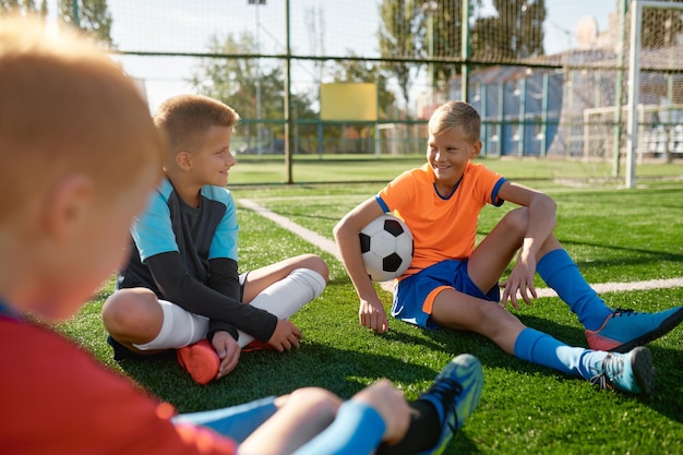 Équipe de football d'adolescents parlant sur le terrain de football se reposant après l'entraînement ou le match