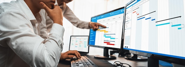 L'équipe de gestion de projet coordonne et met à jour le calendrier prévu du projet sur ordinateur à l'aide d'un logiciel de diagramme de Gantt au bureau Les hommes d'affaires planifient l'heure et la date limite pour la tâche de l'entreprise