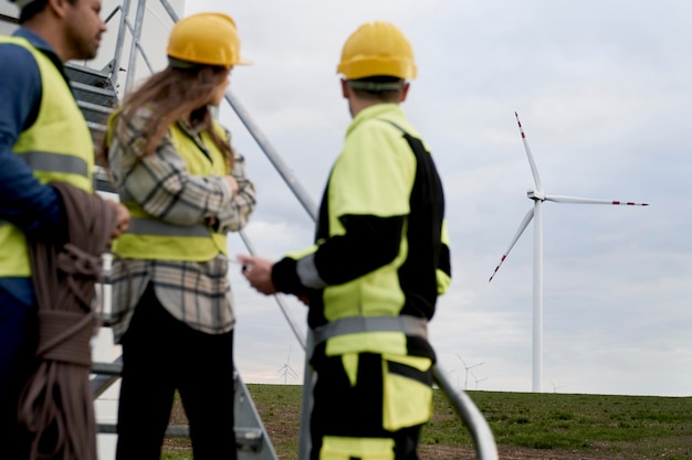 Une équipe d'ingénieurs caucasiens et latins se tiennent sur le champ d'éoliennes et se tournent vers le champ.