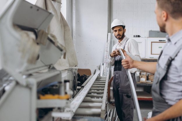 Une équipe internationale deux ouvriers travaillent sur une machine dans une usine de portes et fenêtres en PVC