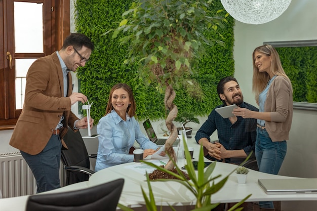 Une équipe de jeunes ingénieurs qualifiés et intelligents discutant du projet d'énergie alternative et l'un d'eux tenant le petit modèle de turbine éolienne et expliquant son fonctionnement.