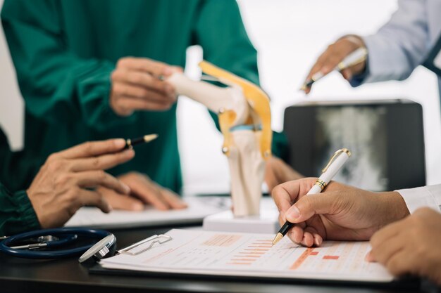 une équipe de médecins sérieux analyse un modèle de fracture du genou montrant le processus des patients souffrant d'arthrose et d'arthroplastie du genou