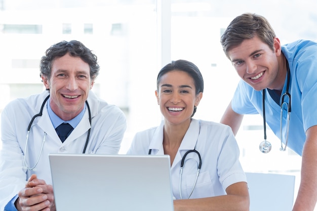Équipe de médecins travaillant sur ordinateur portable et souriant à la caméra