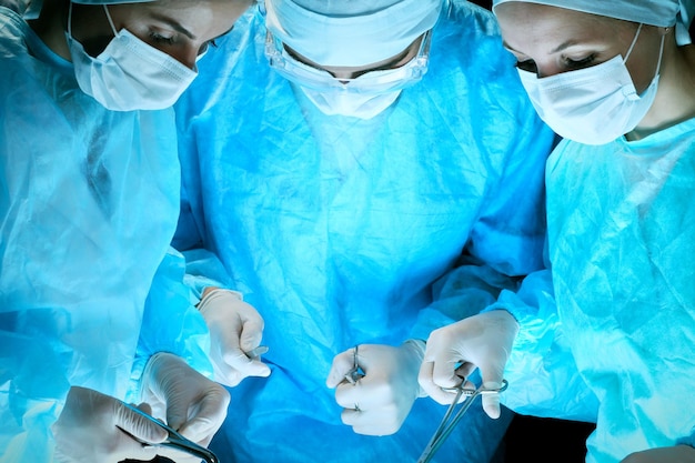 Photo Équipe médicale effectuant une opération. groupe de chirurgiens au travail en salle d'opération en bleu.