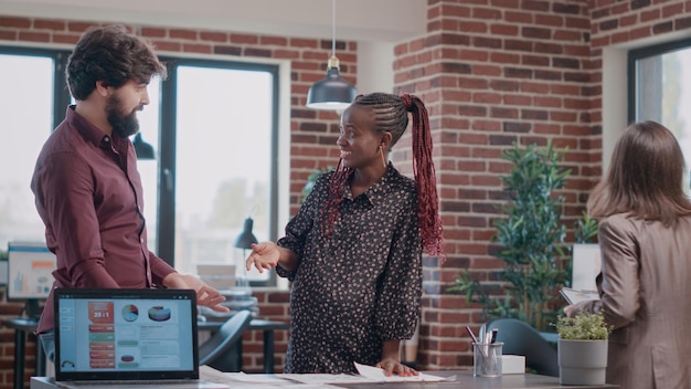 Photo Équipe multiethnique de personnes donnant highfive tout en travaillant sur un projet d'entreprise. une femme attend un bébé et travaille en équipe avec un collègue pour concevoir des graphiques sur des documents. employée enceinte