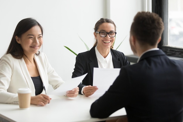 Une équipe de ressources humaines multiraciale positive ou des cadres féminins sympathiques riant d'une blague amusante lors d'un entretien d'embauche réussi avec un candidat masculin gagnant faisant une bonne première impression d'humour et de concept d'embauche