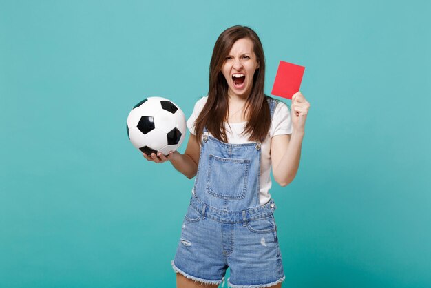 L'équipe de soutien des fans de football d'une jeune femme en colère avec un ballon de football, un carton rouge, propose au joueur de se retirer du terrain isolé sur fond bleu turquoise. Émotions des gens, concept de loisirs sportifs en famille.