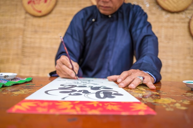 Un érudit vietnamien portant Ao Dai écrit de la calligraphie Le festival de calligraphie est une tradition populaire pendant les vacances du Têt Écrire des couplets pour le nouvel an