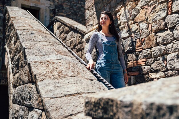 Escalier en décomposition dans un vieux château médiéval historique abandonné. jeune touriste asiatique en salopette descendant des escaliers en pierre visitant l'ancien palais à l'extérieur par une journée ensoleillée tenant la corde.