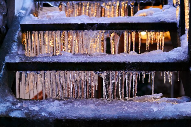 Escalier extérieur au crépuscule du soir recouvert de glace et de glaçons éclairés par une fenêtre derrière elle