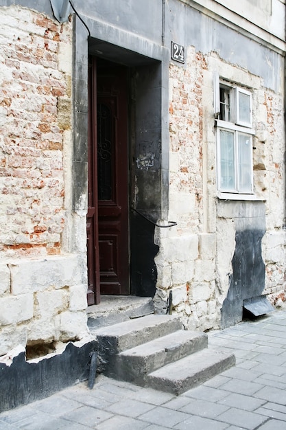 Un escalier et une porte ouverte menant à une vieille maison en brique. Il y a une fenêtre à côté de la porte