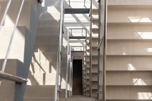 Escaliers dans un immeuble de bureaux en béton dans des tons neutres recouverts de carreaux de céramique avec garde-corps en métal brillant