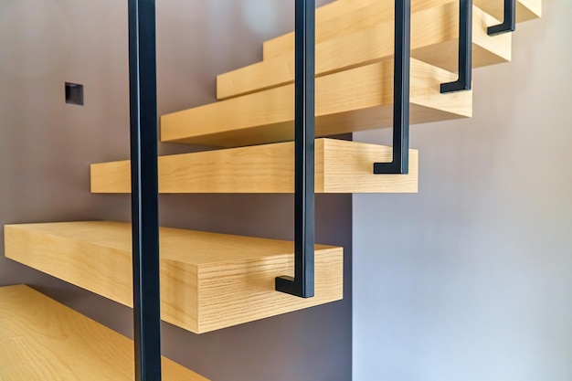 Escaliers flottants Escaliers en bois de frêne avec garde-corps en métal fixé au mur marron et menant au deuxième étage à l'intérieur d'une maison moderne et élégante