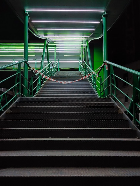 Les escaliers de nuit avec garde-corps en fer sur le pont piétonnier sont éclairés par des lanternes vertes.