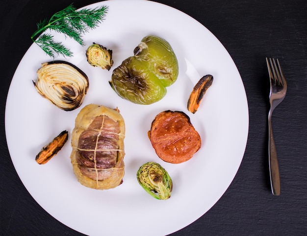 Escalope de viande avec légumes grillés sur une plaque blanche et sur un fond sombre