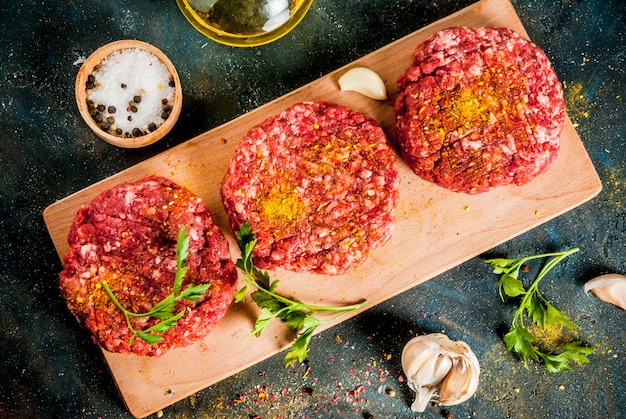 Escalopes de burger crues avec sel, poivre, huile, herbes et épices, sur table sombre, copy space