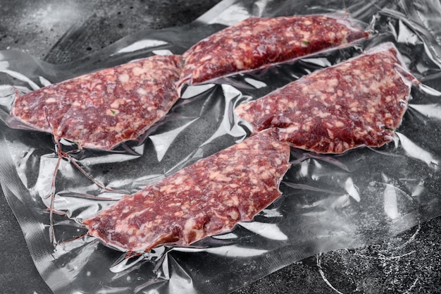 Escalopes de veau de boeuf dans un emballage en plastique sous vide sur fond de table en pierre noire foncée