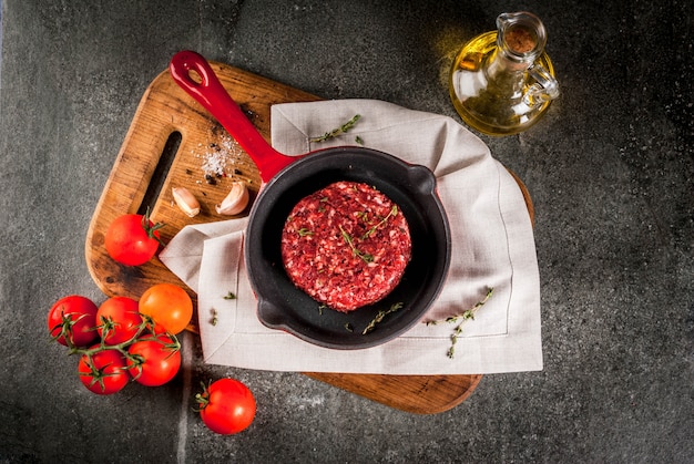 Escalopes de viande de boeuf bio crue avec des épices, du thym, des tomates, de l'huile d'olive dans une poêle sur fond noir, copyspace vue de dessus