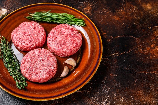 Escalopes de viande de hamburger crue avec du boeuf haché et des herbes sur une assiette. Fond sombre. Vue de dessus. Espace de copie.