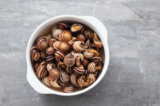 Escargots bouillis dans le bol blanc sur fond en céramique