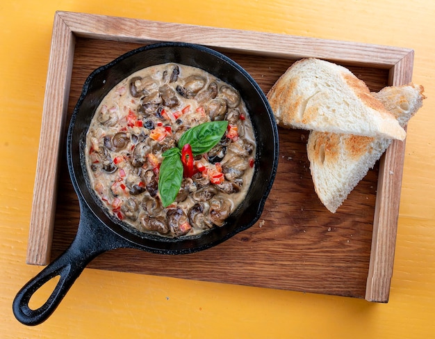 Escargots frits à la crème dans une poêle en fonte Sur un support en bois