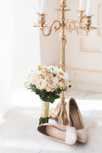 Escarpins à talons hauts beiges avec bouquet de mariage et chandelier au soleil du matin