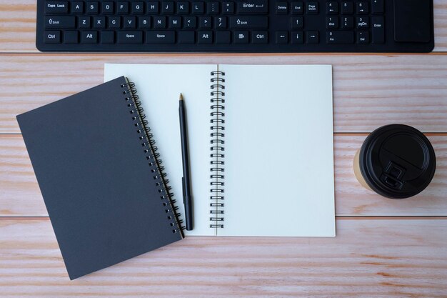 Espace de bureau à domicile avec clavier, cahiers, stylo et tasse à café jetable sur table en bois. Espace pour le texte. Mise à plat, vue de dessus